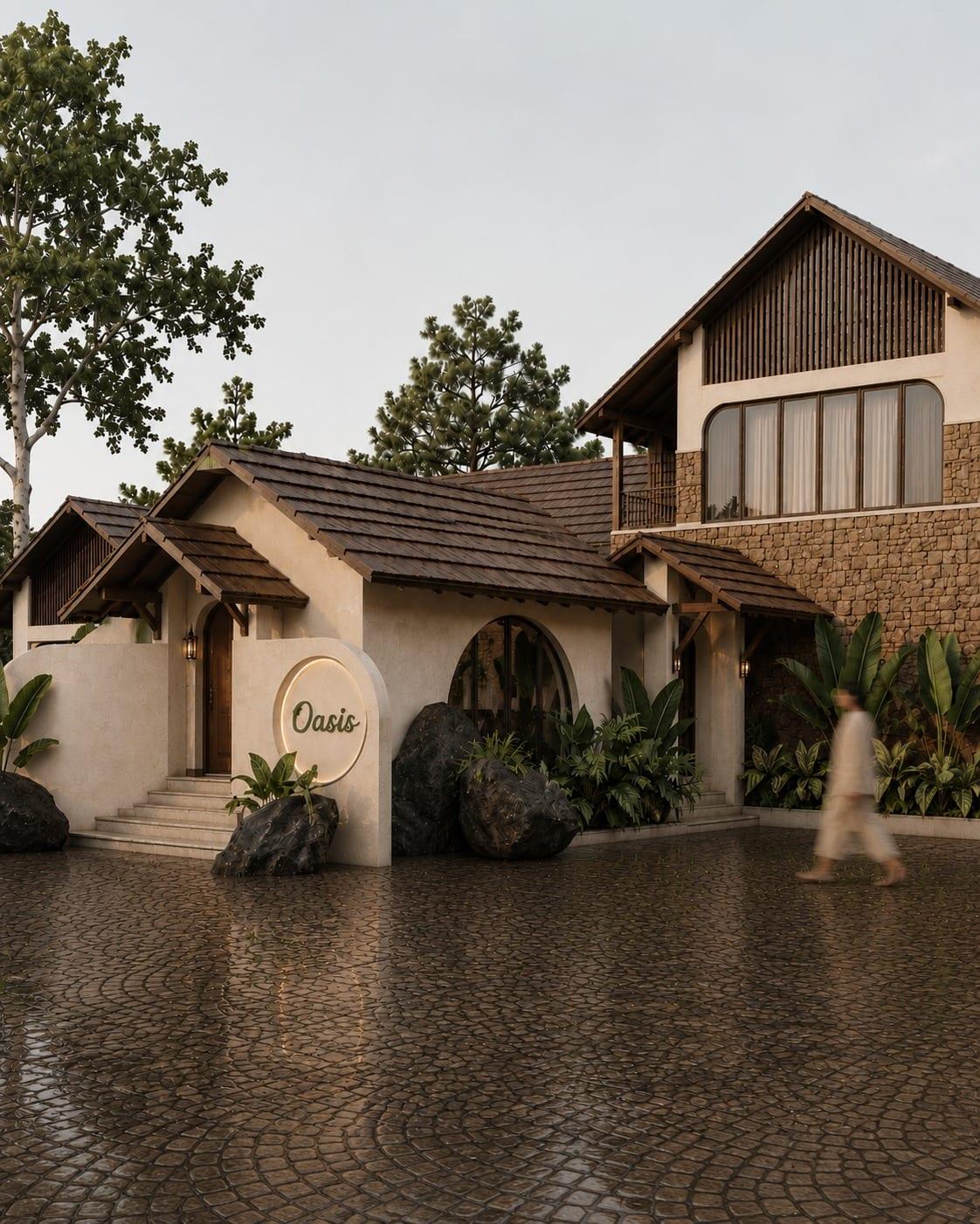 The street elevation in soft evening light: layered tiled roofs, an arched window, random stone cladding on the upper floor and boulders set among tropical planting
