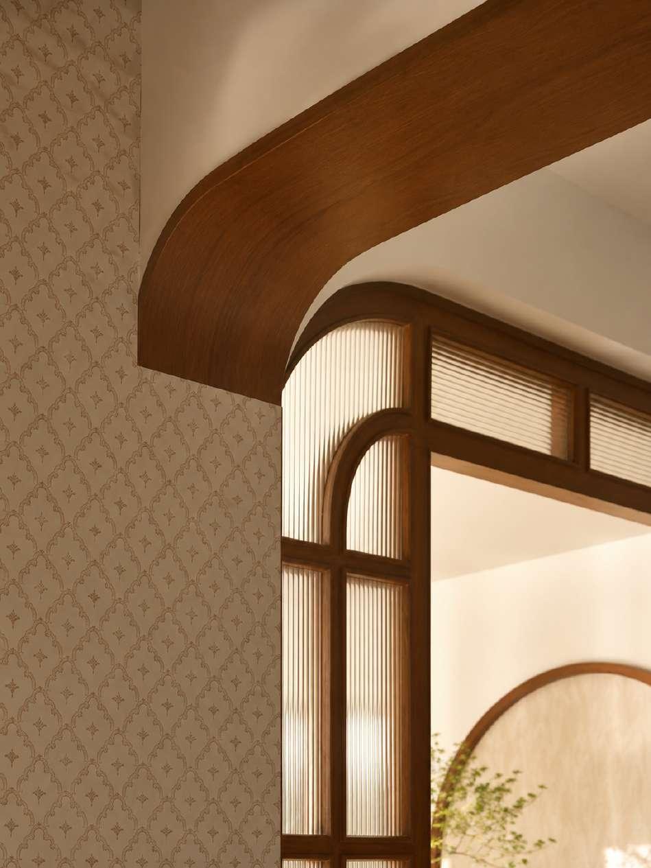 A sweeping curved teak cornice meets an arched fluted-glass partition, with patterned wallpaper in soft ivory
