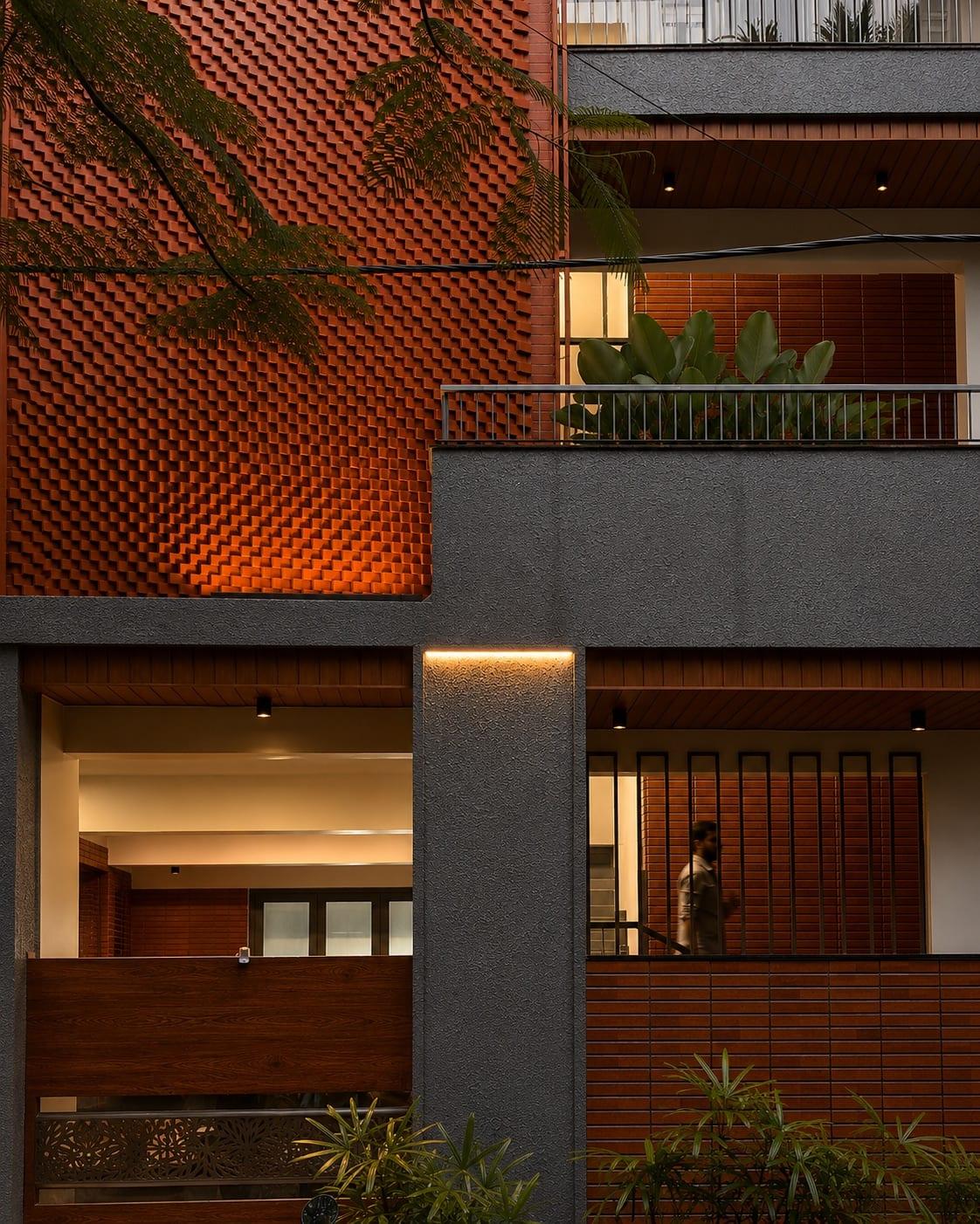 Street elevation with a patterned terracotta brick screen, slate-grey rendered walls, timber soffits and layered planting
