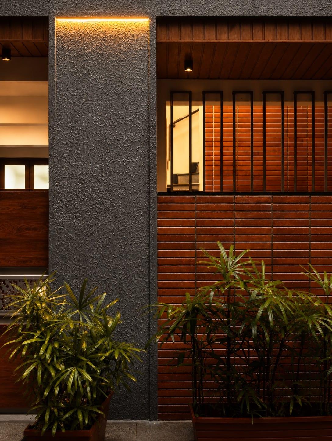 Entrance detail: a textured charcoal column with a concealed light line, teak slat screens and a terracotta-clad wall