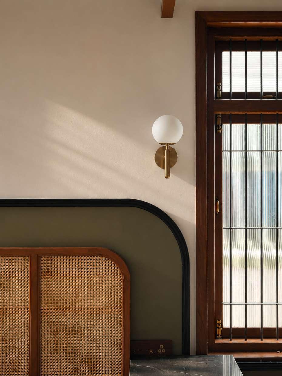 Material palette: cane headboard, olive upholstery, a brass globe sconce and dark teak window frames with fluted glass